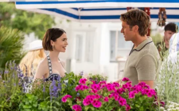 Emily em Paris chega à última temporada; Netflix divulga primeiras imagens e novidades "A woman and man talk and smile at an outdoor flower market, standing among vibrant purple flowers and green plants under a striped canopy, with a white building in the background."